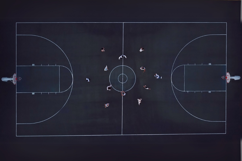 Aerial shot photo of people dancing in a circle on a basketball court.